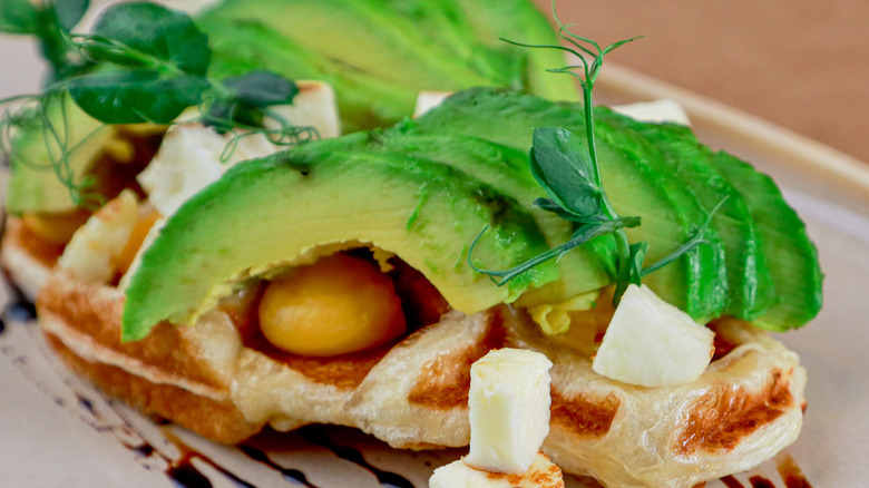 A Belgian waffle is topped with avocado, cream cheese and herbs.