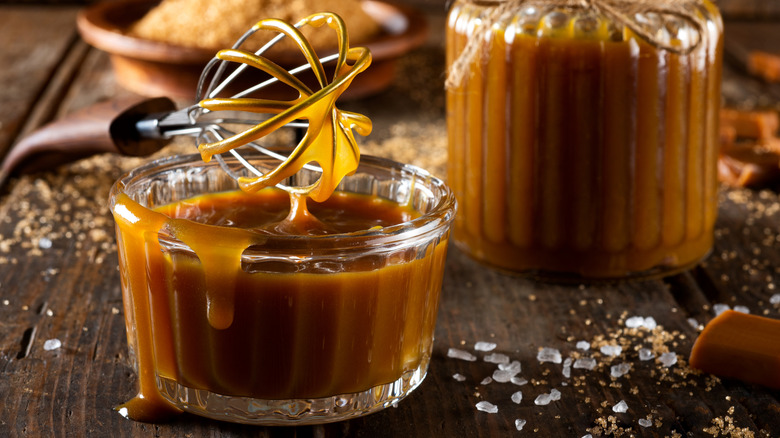 A homemade salted caramel sauce﻿ sits in a small glass bowl with a whisk.