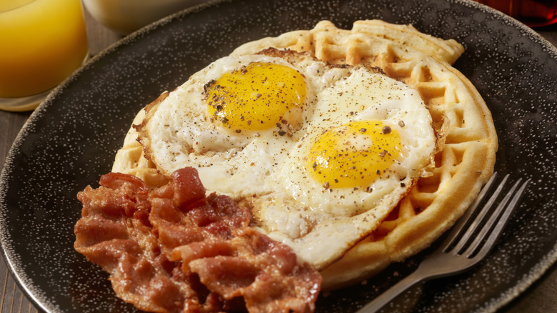 A fried egg and bacon sit on a waffle.