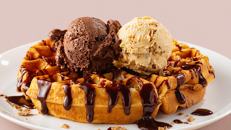 A Belgian waffle has ice cream gelato scoop and chocolate sauce on top.