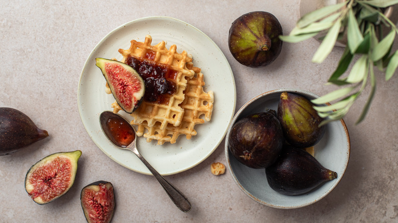 A waffle has fig jam spread on top and figs on the side.