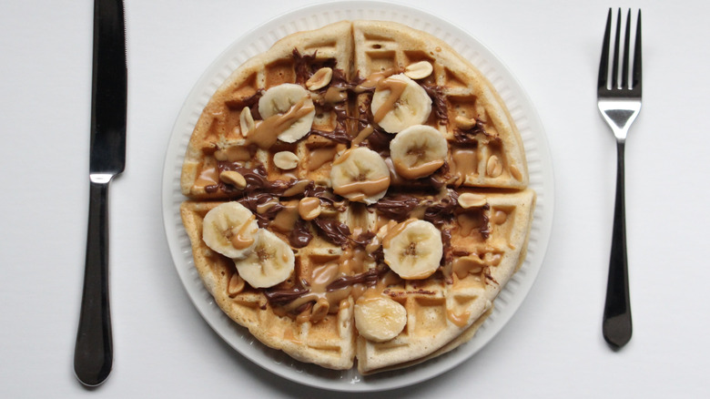 Peanut butter is spread on a waffle with bananas and chocolate sauce.