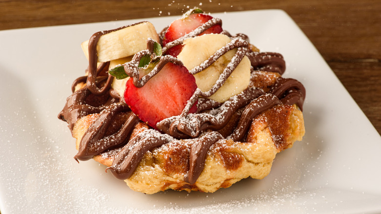 A Belgian waffle is topped with Nutella, strawberries, and bananas.