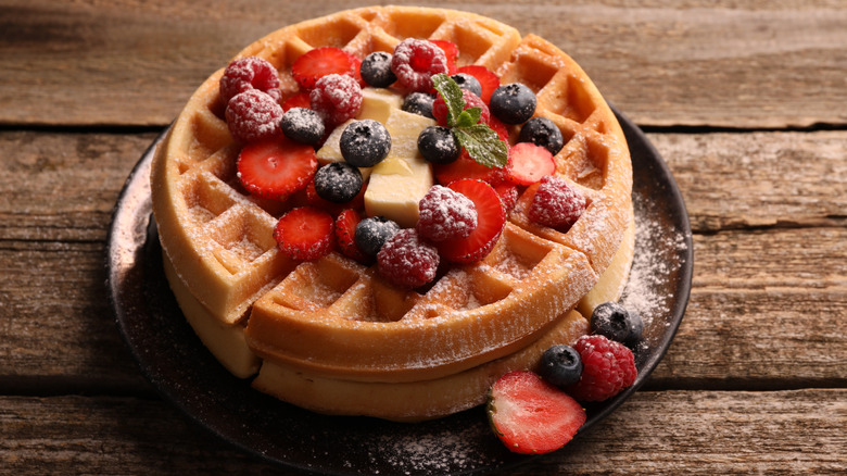 A waffle has powdered sugar and fruit on top.