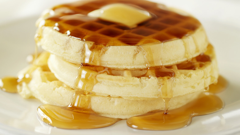 A stack of waffles is topped with butter and maple syrup.