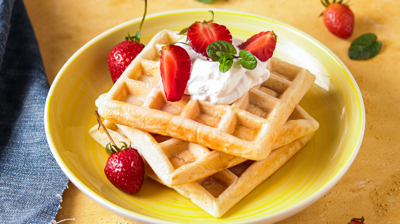 Waffles and strawberries with whipped cream sit on a yellow plate.