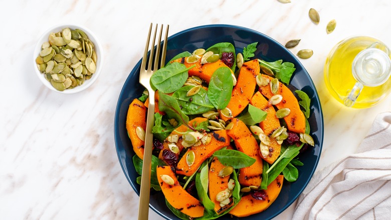 Grilled pumpkin salad in bowl with spinach leaves and pepitas