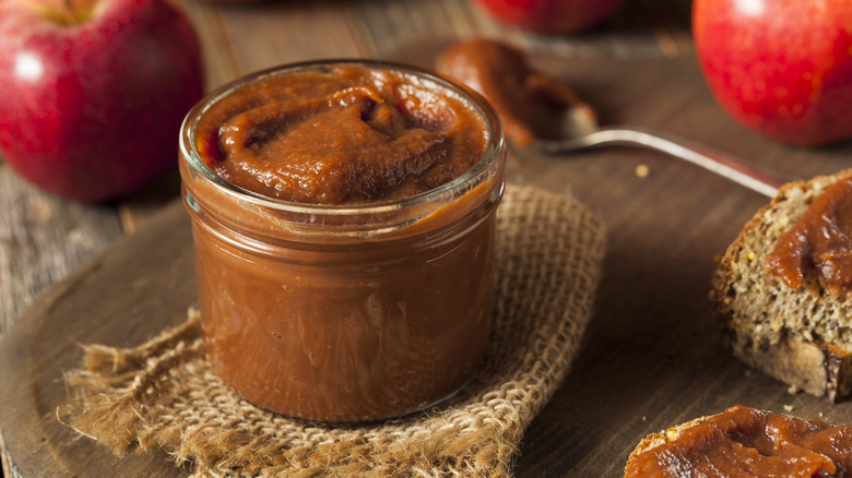 Apple butter in glass jar surrounded by fresh apples