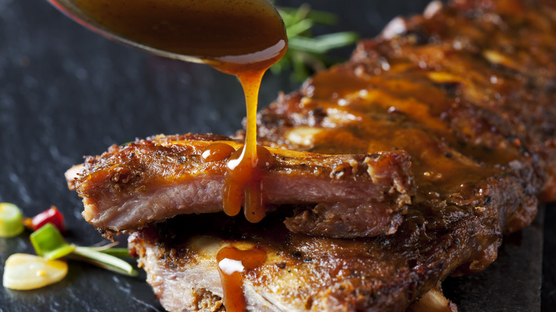 Spoon pouring red sauce over cooked ribs