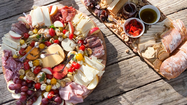 Two charcuterie boards with meats, cheeses, breads, and fruits on wooden table