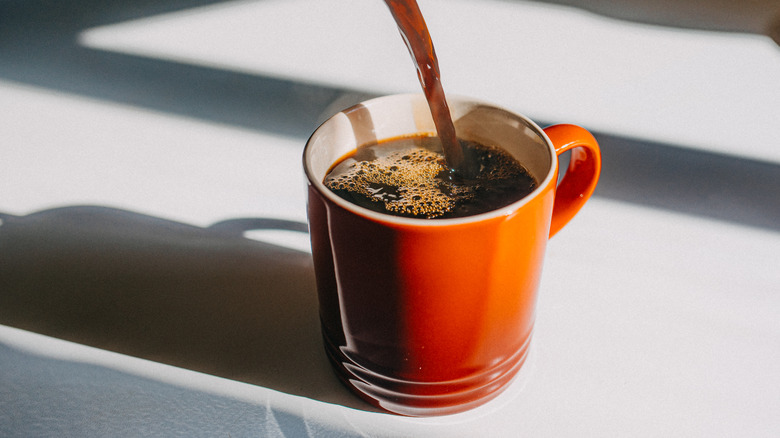 stream of coffee being poured into red coffee mug