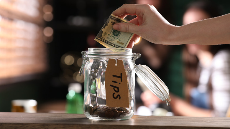 Hand putting money in tip jar