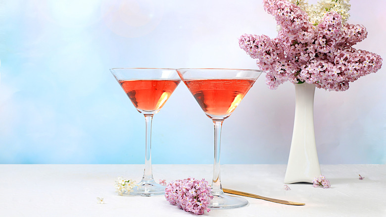 Festive alcoholic cocktail red martini in glasses on a bright background with a bouquet of lilacs.