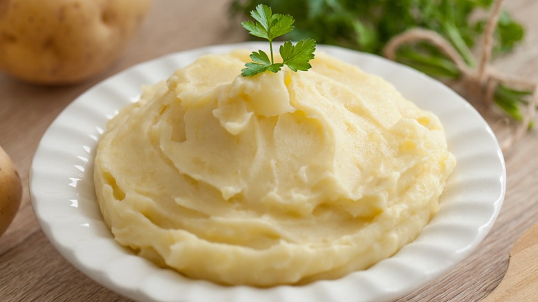 Mashed potatoes in white bowl on table with parsley garnish