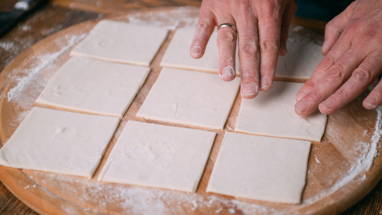 Person's hands working with puff pastry on wooden surface