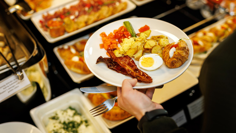 Guest picks up different food at hotel breakfast buffet