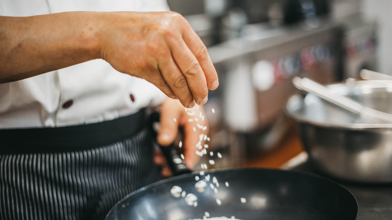 Chef sprinkles rice into pan