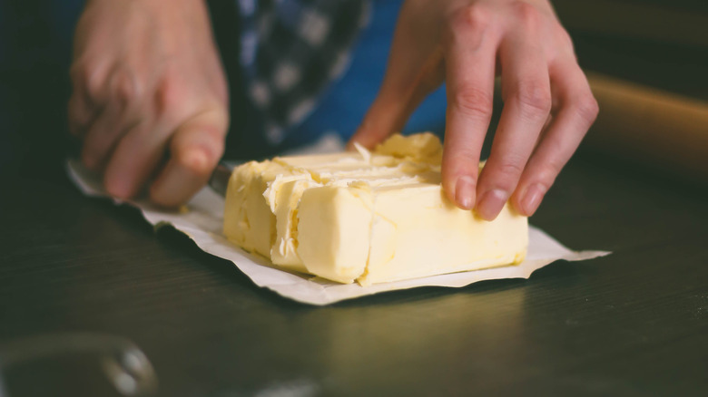 Hands cutting butter with knife