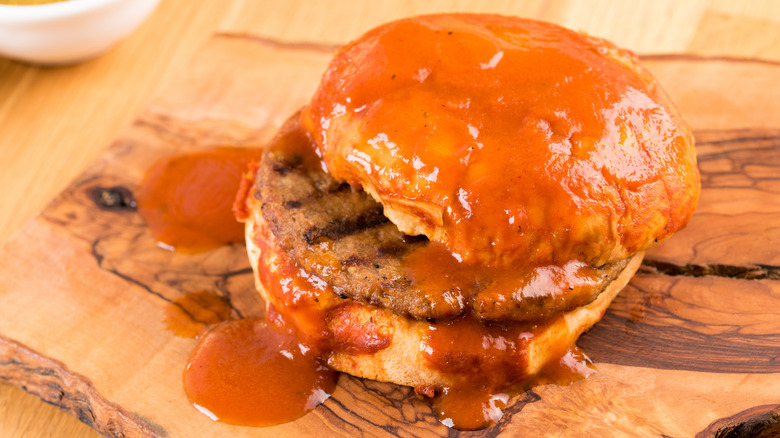 Burger covered with sauce on wooden board 