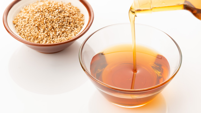 Sesame oil and seeds in bowls on white background