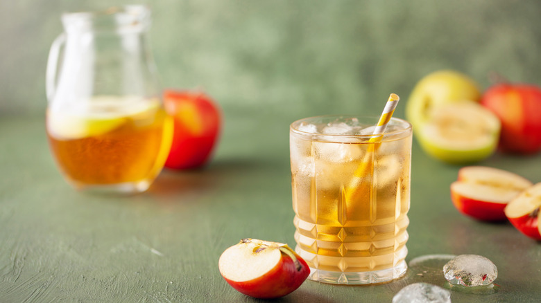 glass of apfelschorle with paper straw surrounded by apples
