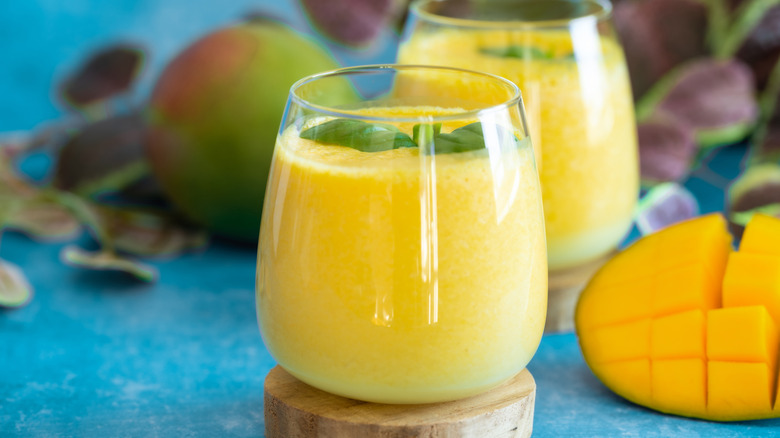 Two glasses of mango lassi surrounded by mangoes