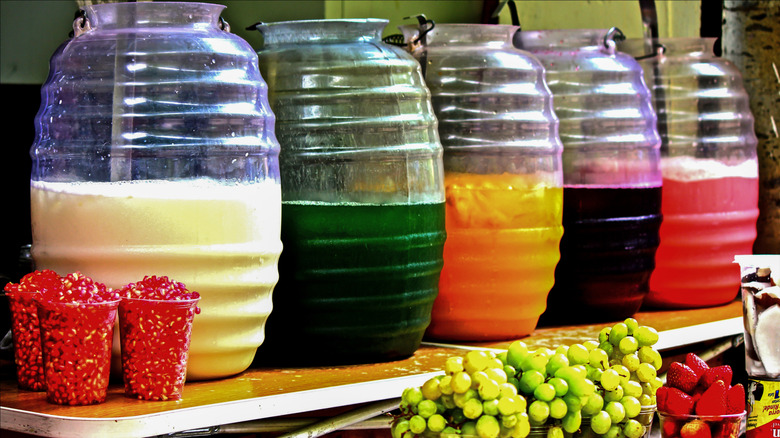 Containers of agua fresca next to fruits