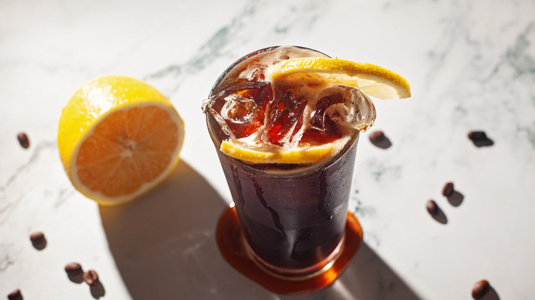 glass of mazagran with halved lemon on marble surface