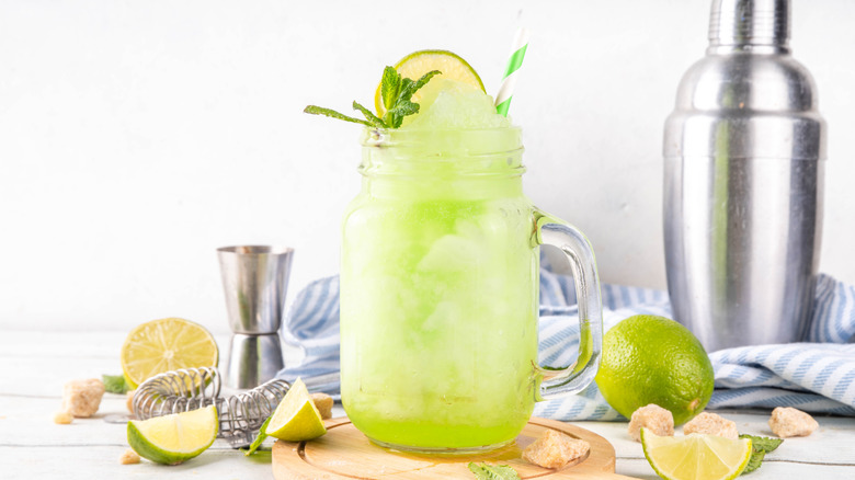 glass of limeade surrounded by shaker and limes
