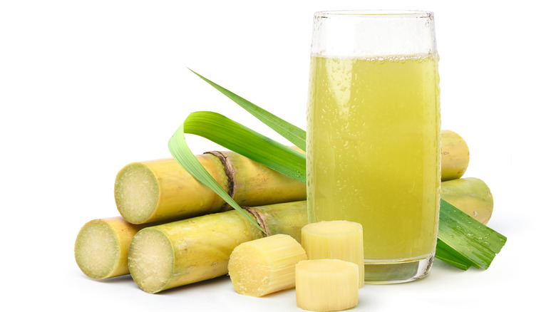 A glass of sugarcane juice next to chopped sugarcanes