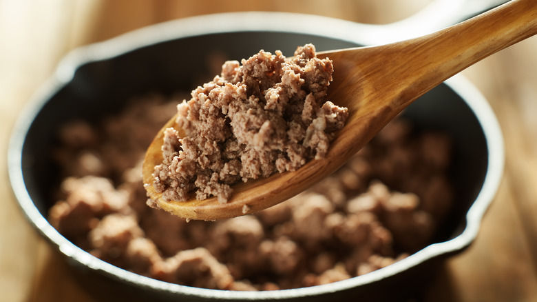 Cooked ground meat in a wooden spoon with a pan in the background