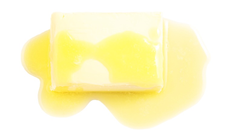 A block of yellow butter, partially melted on a white background