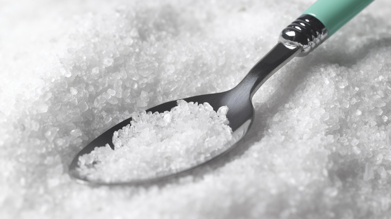 A metal spoon filled with salt crystals, dipped in a heap of salt spread in the background