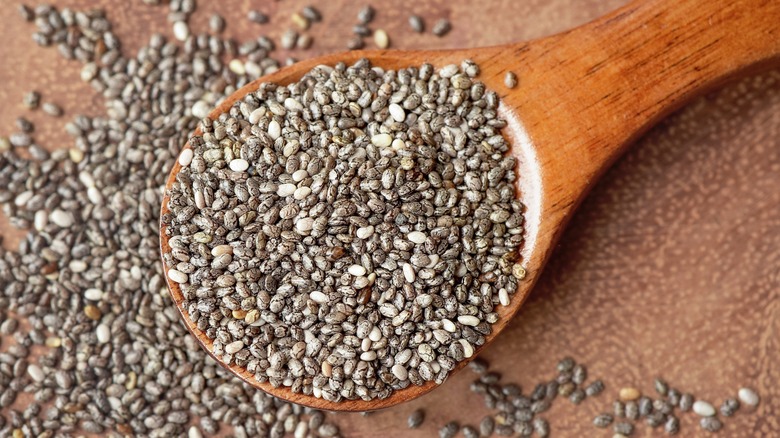 Chia seeds in a wooden spoon with many chia seeds spread on a wooden background