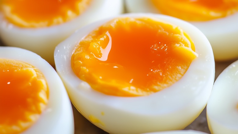 A close-up of halved soft-boiled eggs with runny yolk in the center, and many eggs in the background