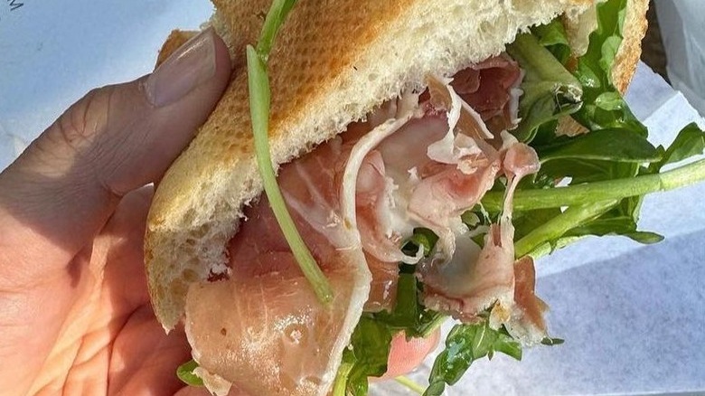 Hand holding prosciutto sandwich