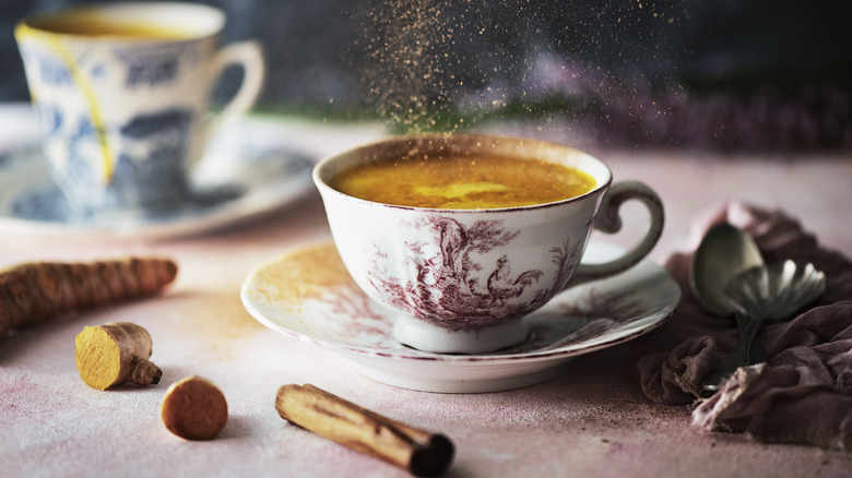 A cup of coffee surrounded by ginger and cinnamon with spices falling through air