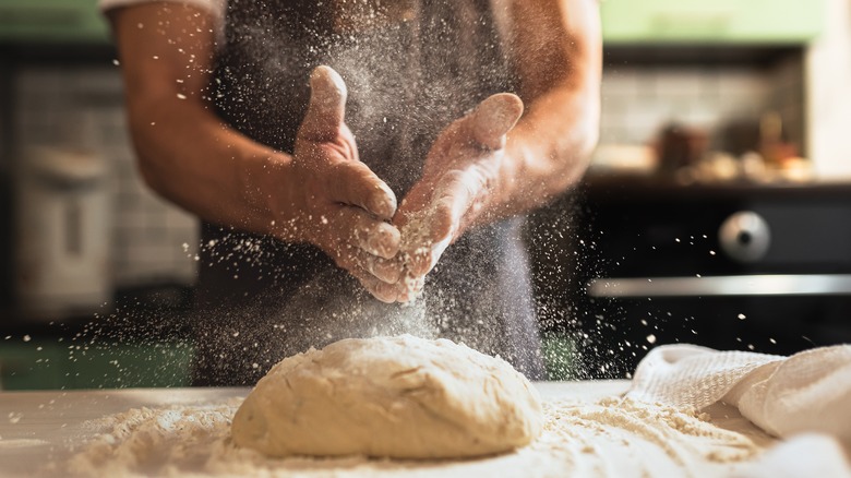 Hands sprinkling flour on dough