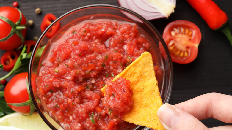 Person dipping tortilla chip into salsa bowl
