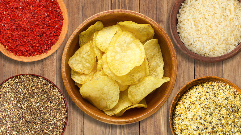 Wooden bowl of potato chips surrounded by different dishes of seasoning and ingredients