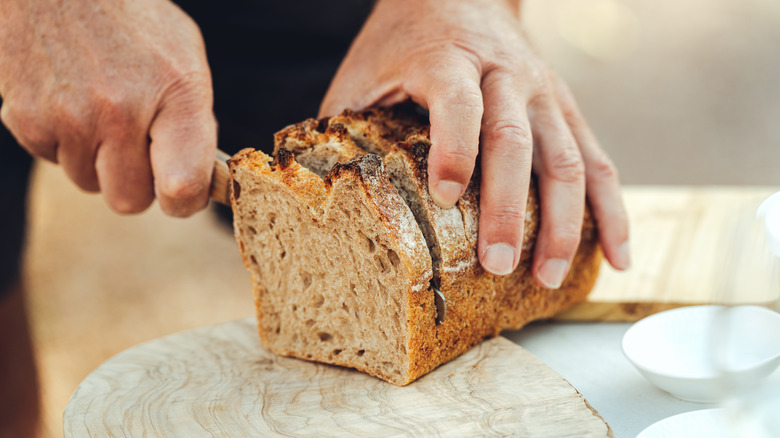 Person slicing bread loaf counter