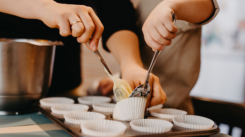 Hands filling cupcake tin