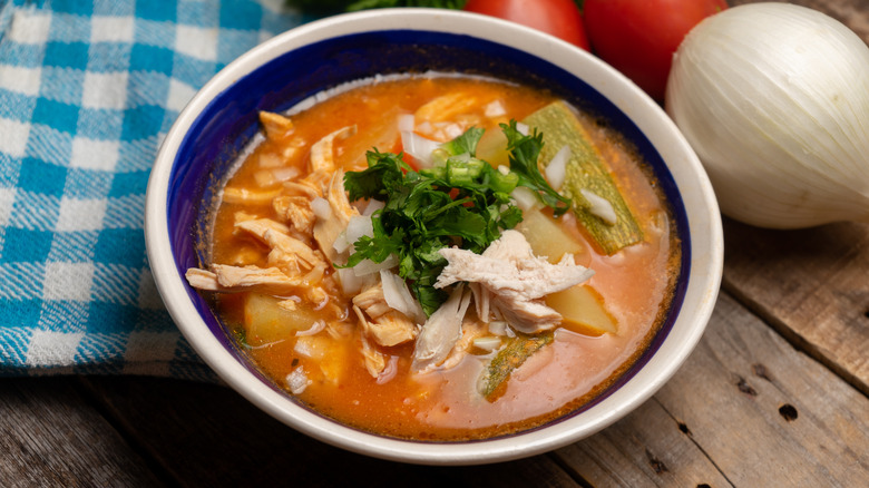 blue bowl with spicy red chicken soup and vegetables