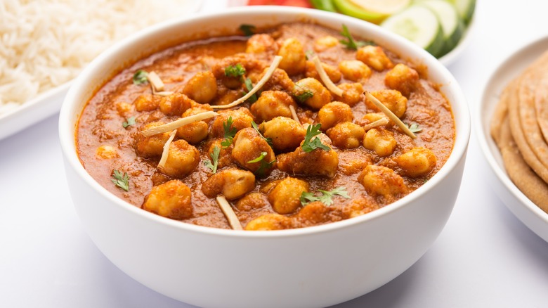 Chickpea curry chana masala in a white bowl with white rice, naan, and veggies