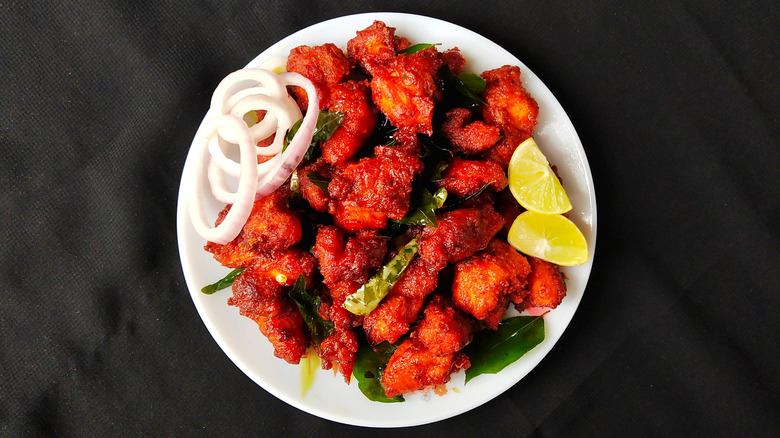 Deep-fried spiced chicken with lemon and onions on a white plate