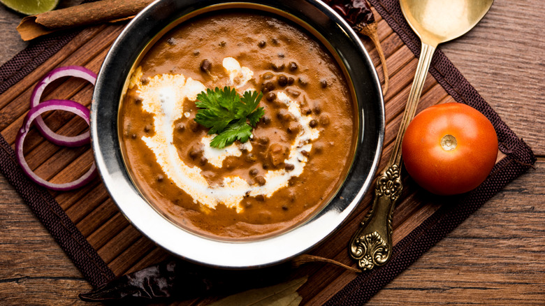 Dal makhani in a metal bowl with additional toppings on a placemat