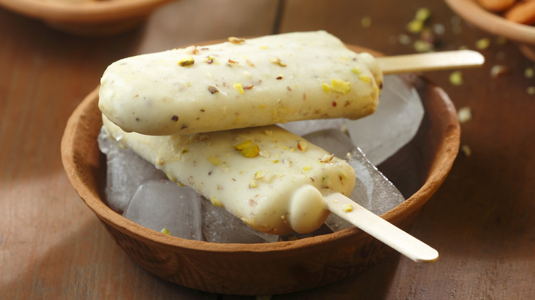 Two pieces of pistachio kulfi sitting over ice in a wooden bowl