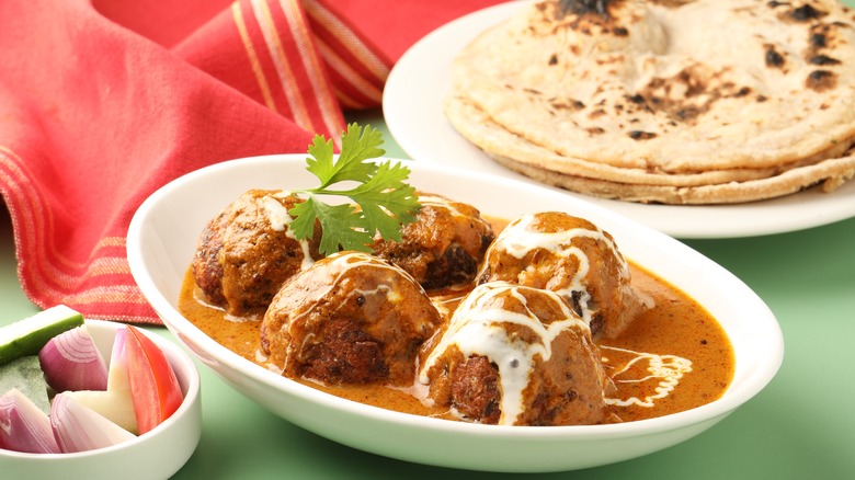 Malai kofta in a white dish with flatbreads