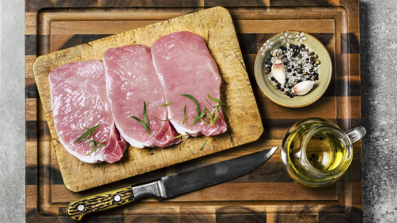 raw pork chops on a cutting board with tarragon leaves and spices