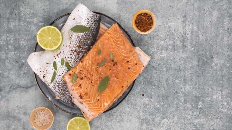 Raw skin-on salmon filets on plate with lemon and herbs